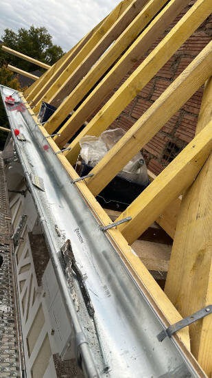 Gouttière posée en rive de toit pendant une rénovation de toiture, chevrons et liteaux neufs